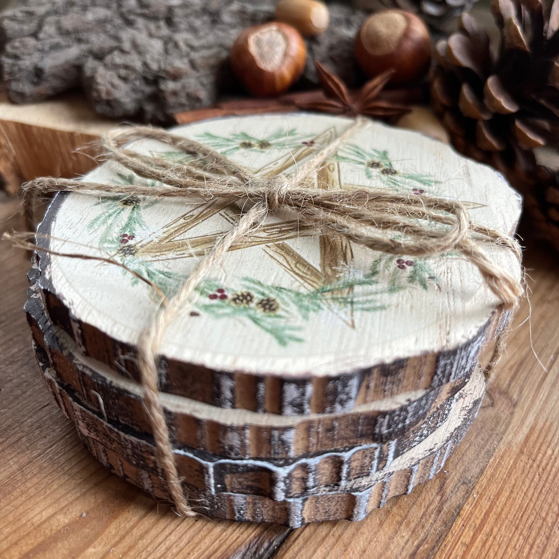 A set of 4 natural wood slice coasters featuring a pretty Winter Solstice wreath and pentagram design. The coasters are elegantly tied with natural string.Shown on a wooden table with natural seasonal symbols in the background such as pine cones, nuts and seeds and holly 