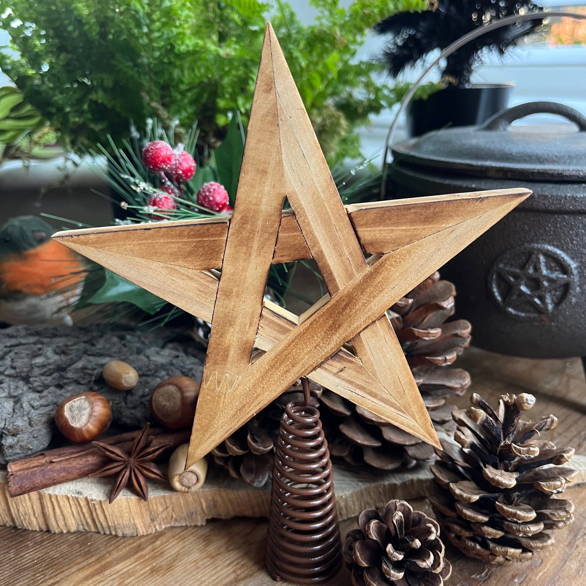 natural wooden Tree Topper in the shape of a pentagram star, shown with traditional christmas decorations of pine cones, holly and robin in the background 