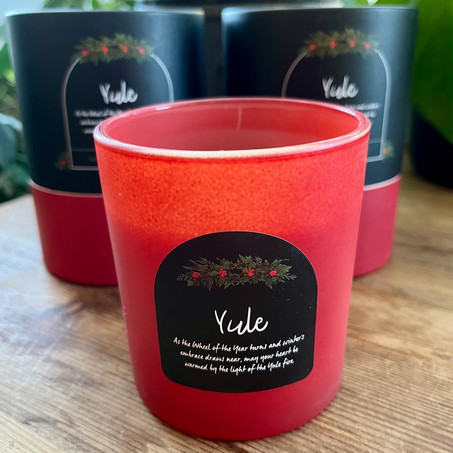 Red candle with 'Yule' label in front of black containers on a wooden surface