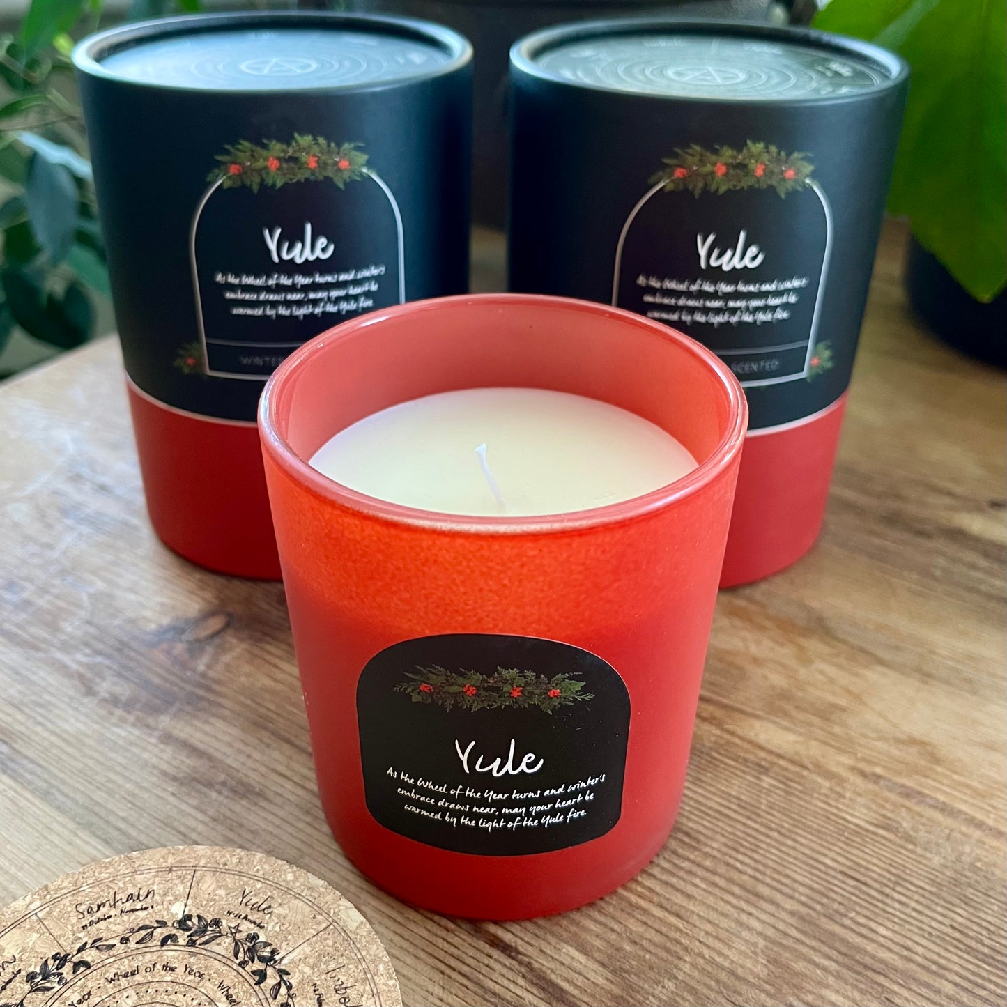 Red candle with 'Yule' label in front of two black candle containers on a wooden surface.