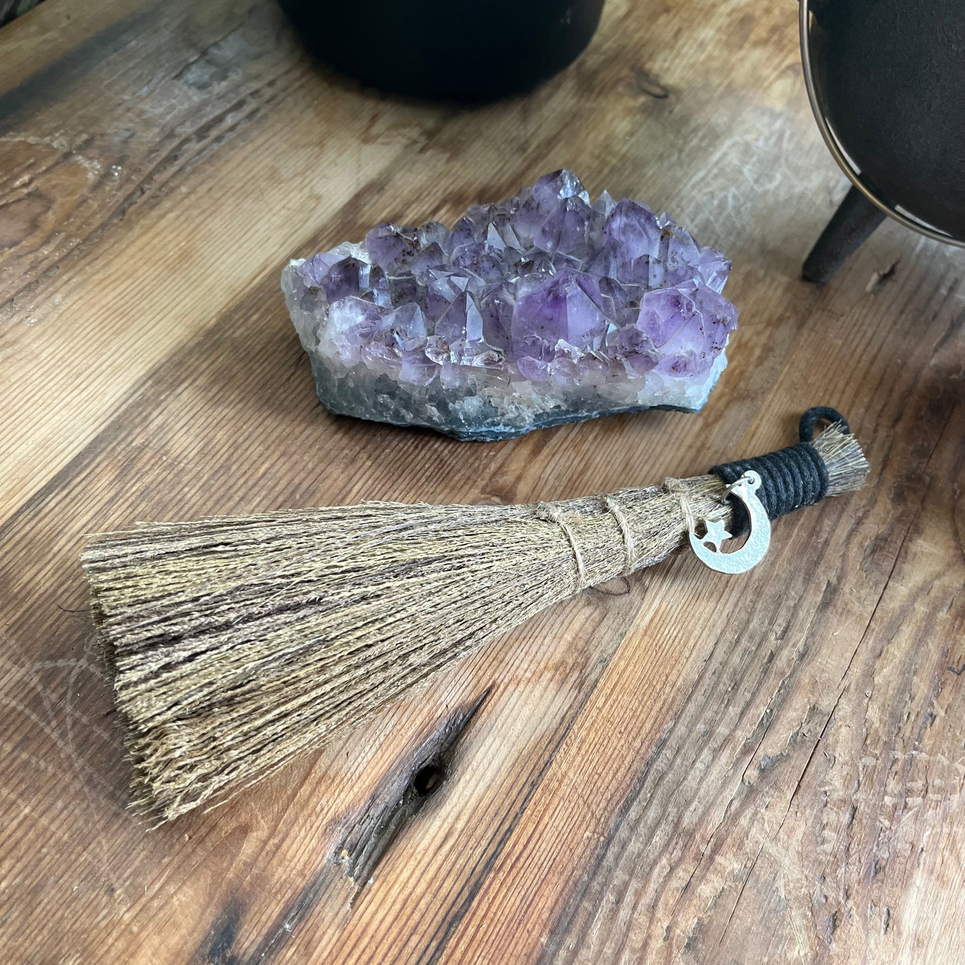 Broom on a wooden surface next to an amethyst crystal.