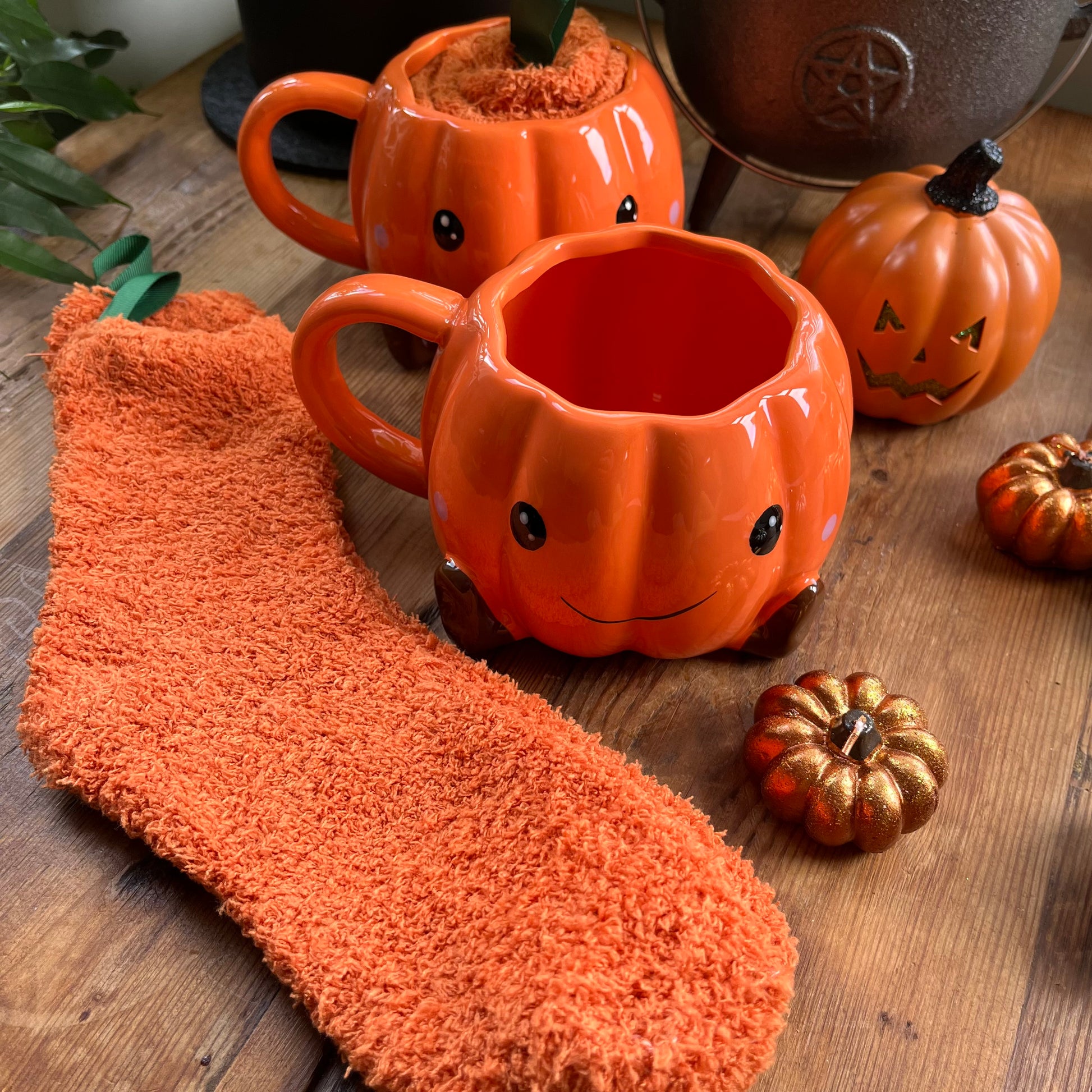 Pumpkin-shaped mugs and decorative pumpkins on a wooden surface with an orange sock.