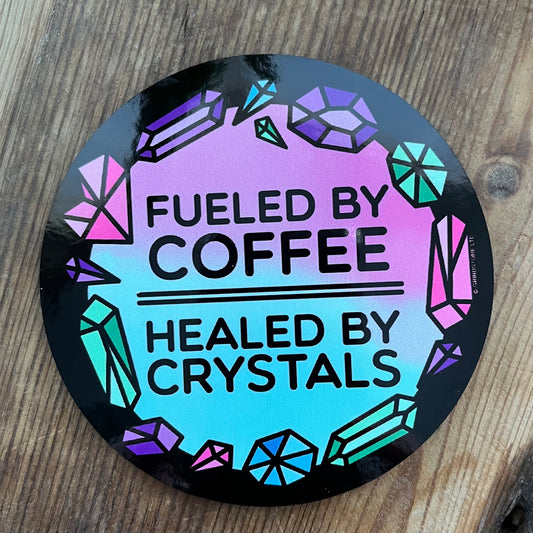 Round coaster with 'Fueled by Coffee, Healed by Crystals' text on a wooden surface