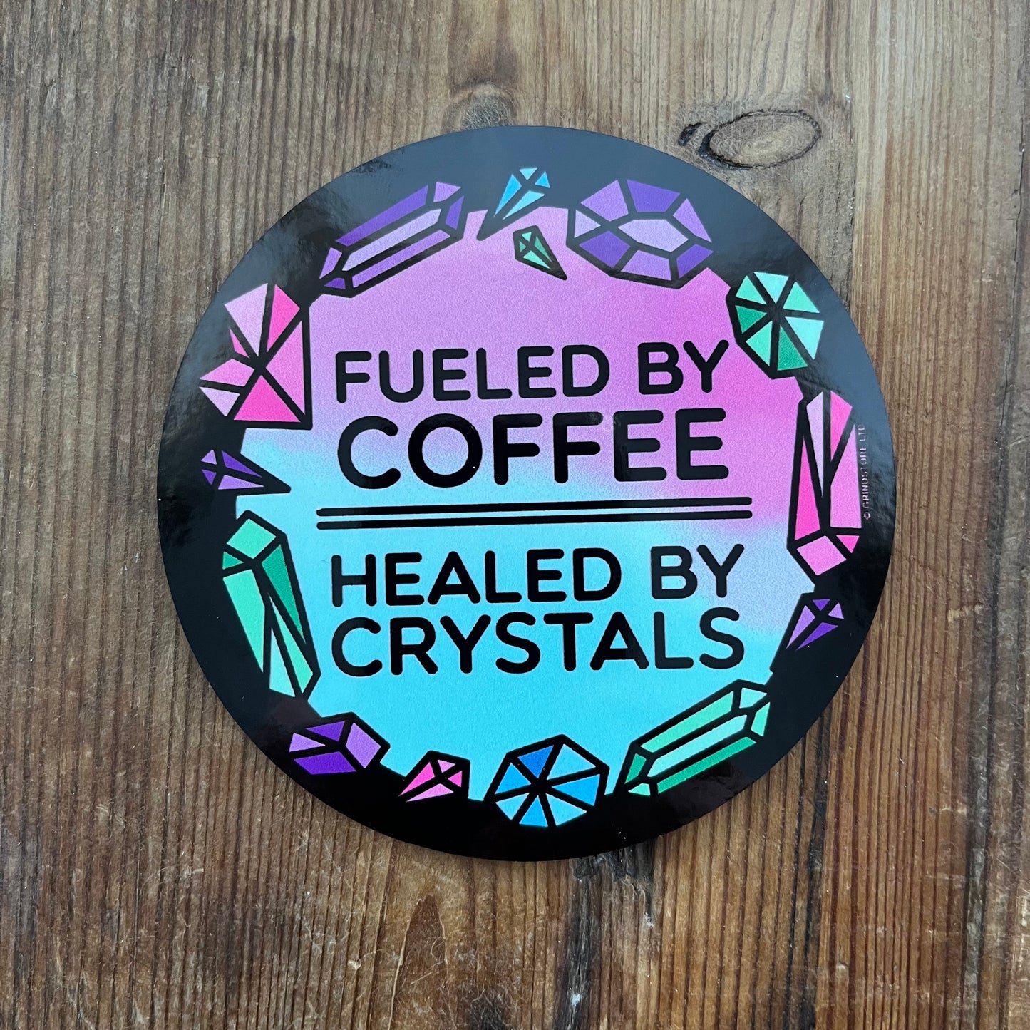 Round coaster with 'Fueled by Coffee, Healed by Crystals' text on a wooden background