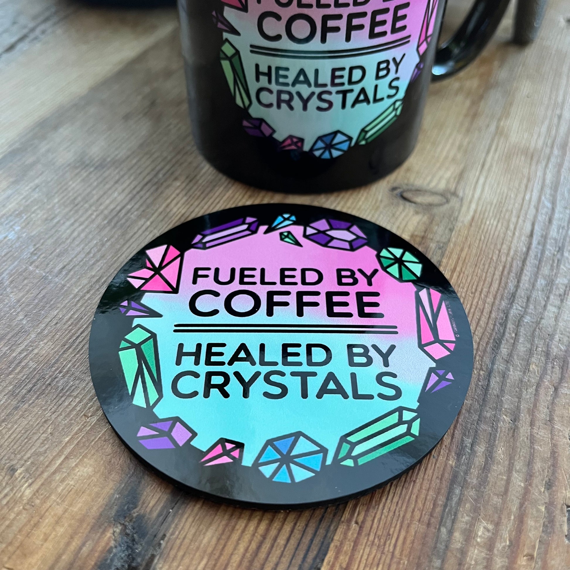 Coaster with 'Fueled by Coffee, Healed by Crystals' text on a wooden surface