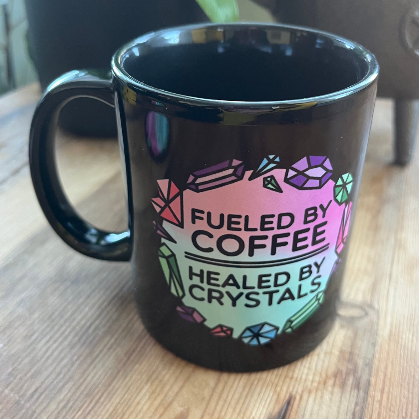 Black mug with colorful coffee and crystals text and gemstone design on a wooden surface