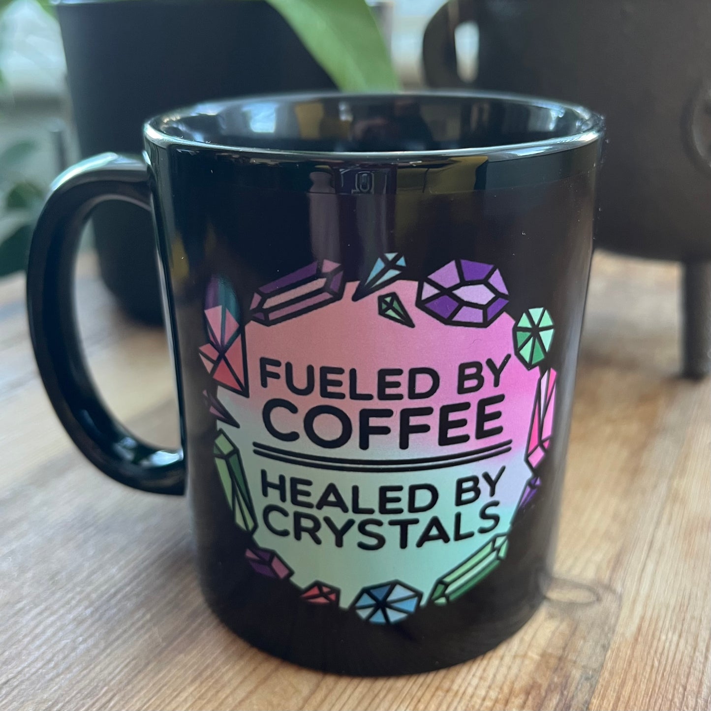 Black mug with colorful text and gemstone design on a wooden surface