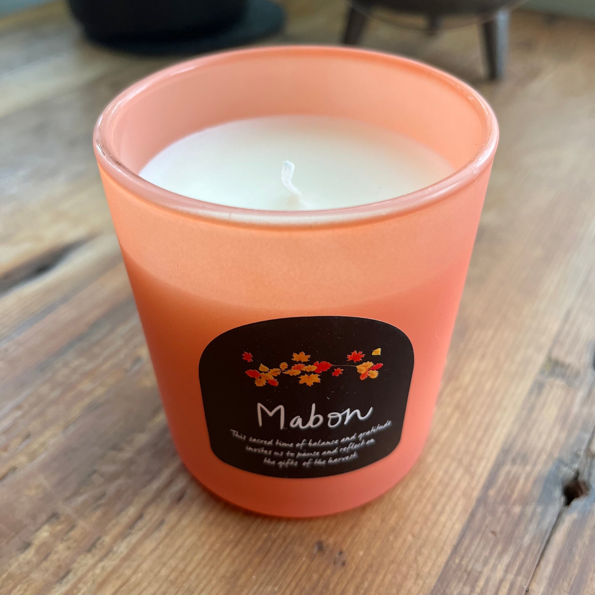 Candle in an orange glass holder with a Mabon decorative label on a wooden surface