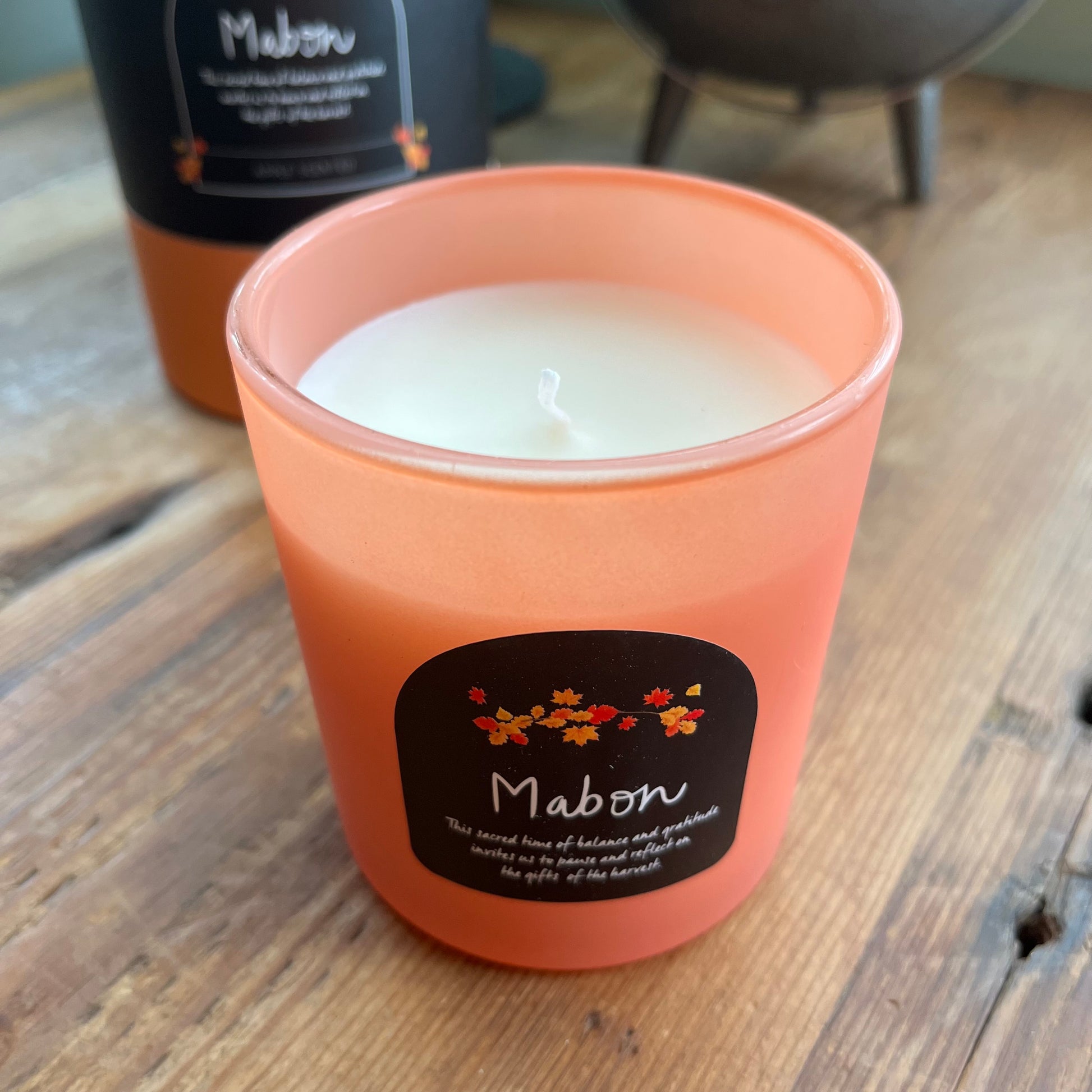 Candle in an orange glass holder with a 'Mabon' label on a wooden surface