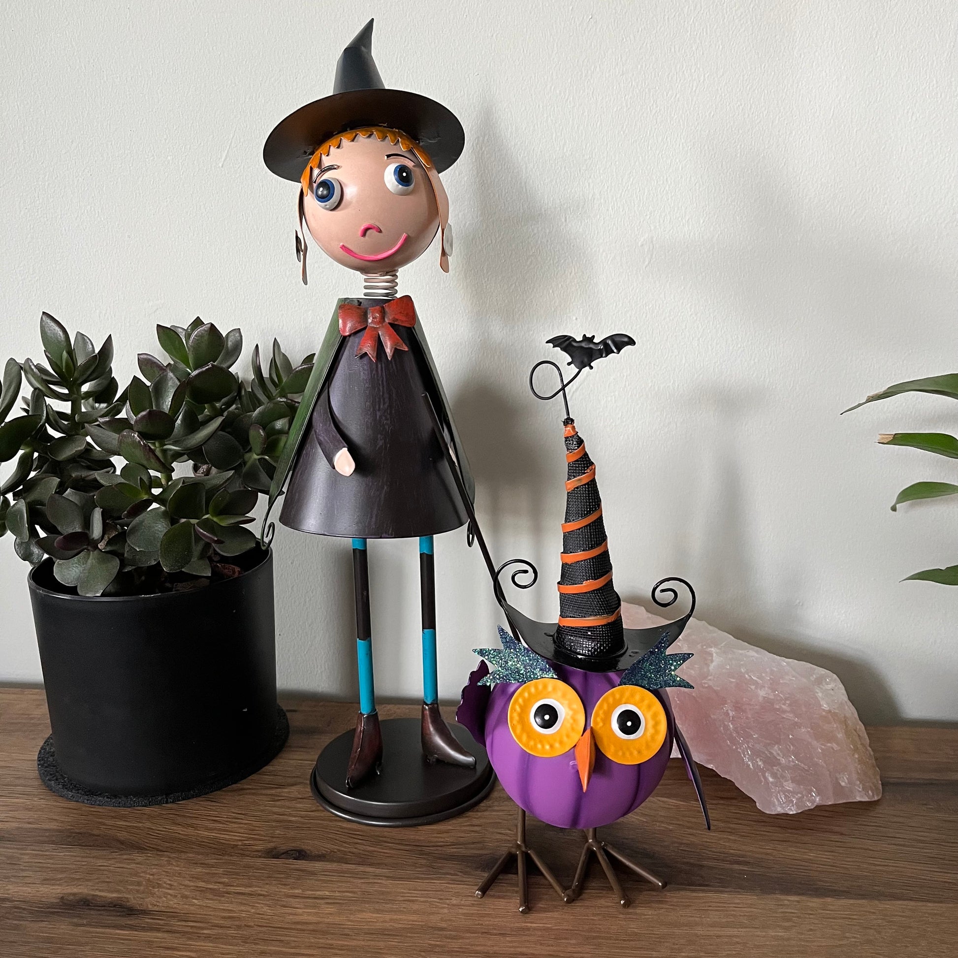 Halloween-themed figurine of a witch and an owl with a bat on a wooden surface.