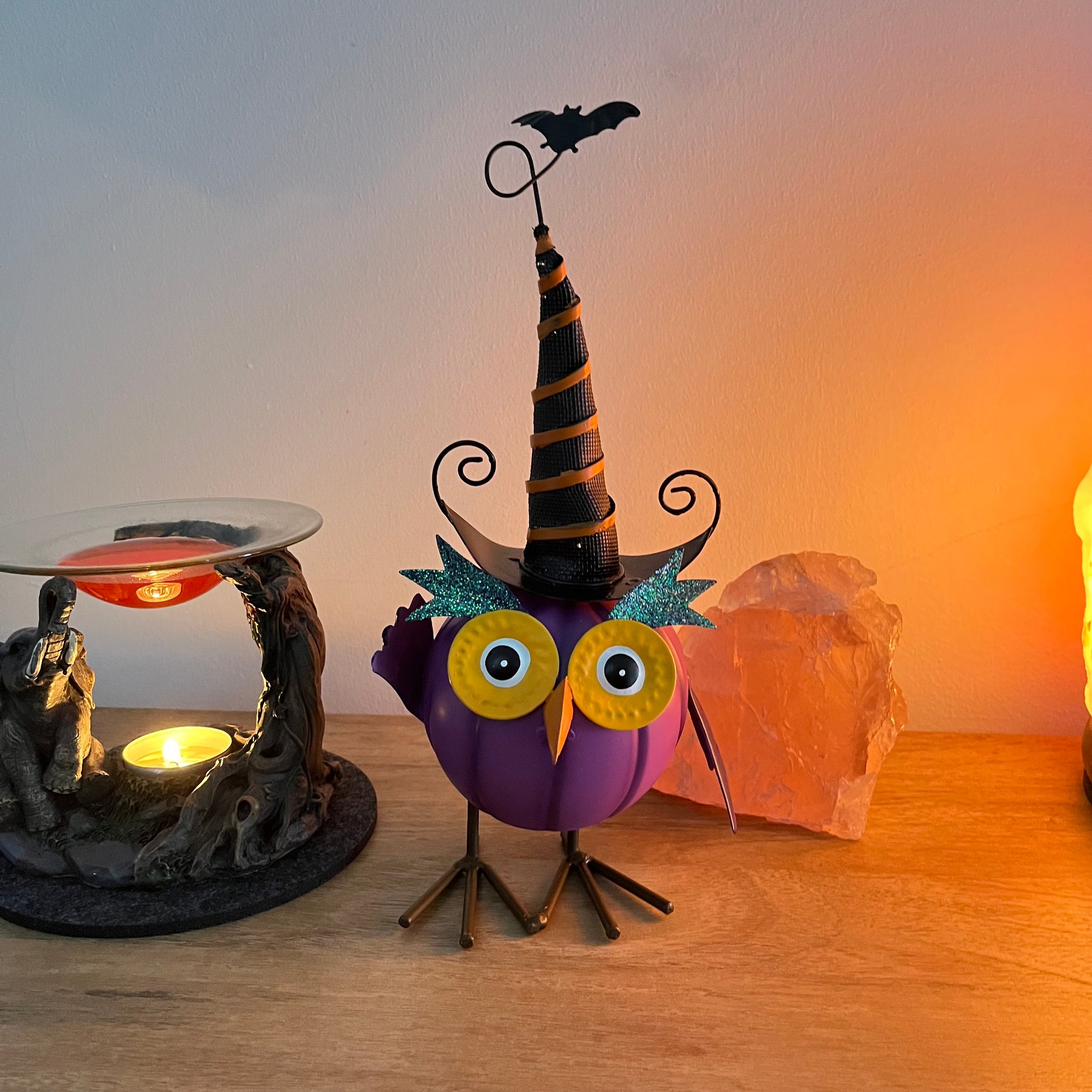 Halloween-themed owl figurine with a witch hat and bat on a wooden surface.