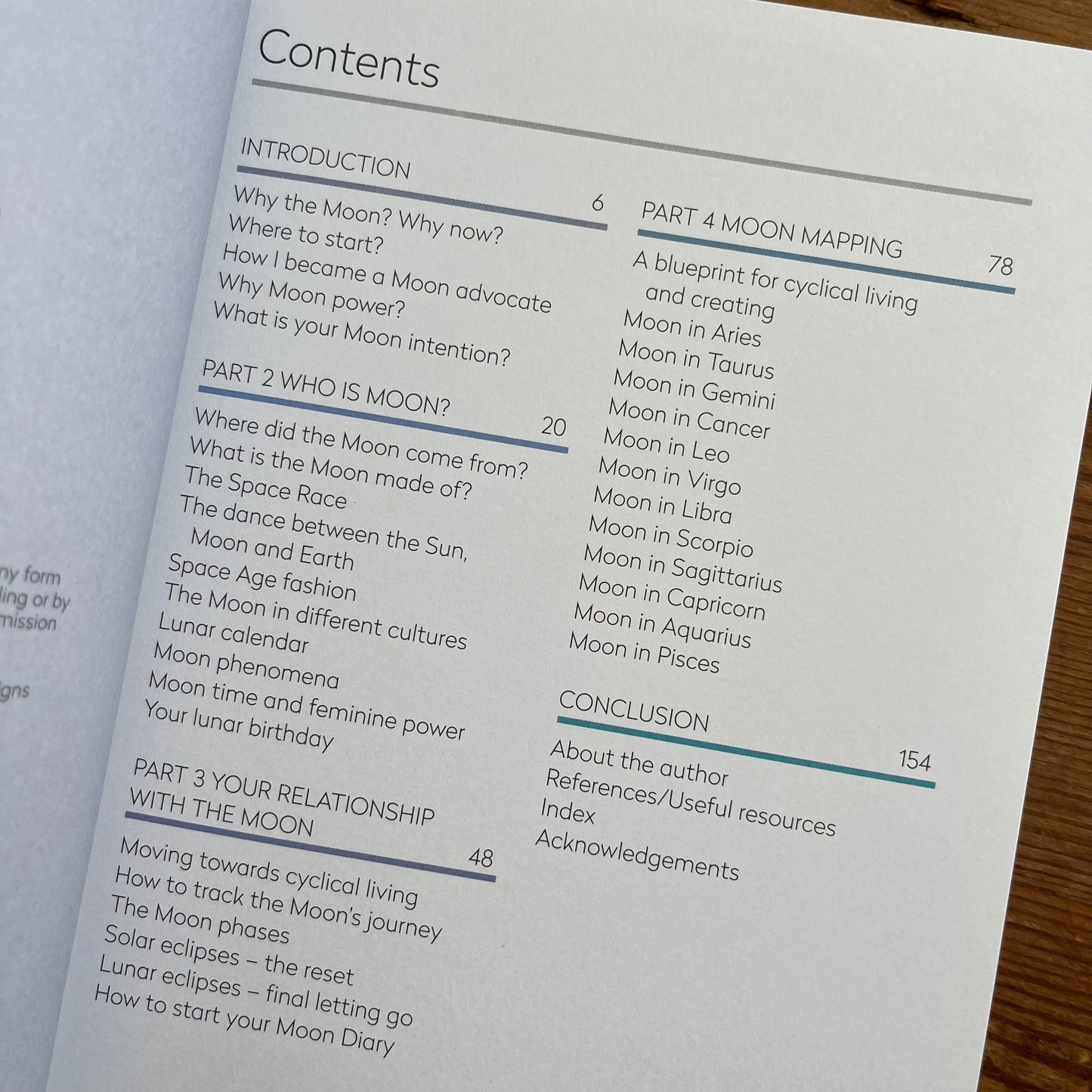 An open book showing the table of contents page, photographed at an angle. The page is white with black text and blue line accents, covering sections from introduction to conclusion.