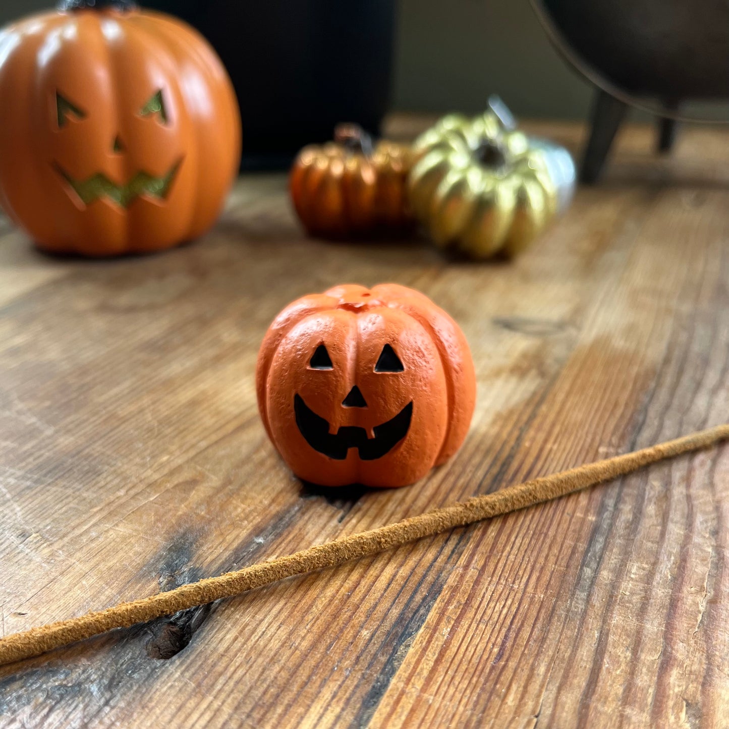 Small orange pumpkin with jack-o'-lantern face on a wooden surface with other pumpkins in the background.
