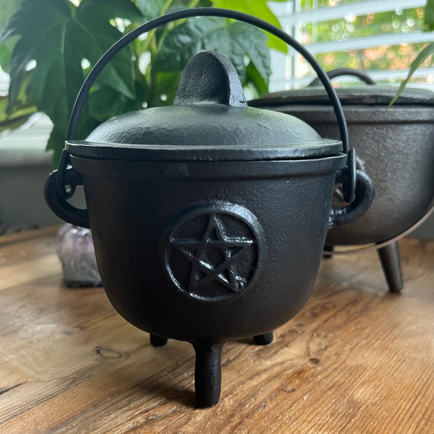 Black cast iron cauldron with a pentagram symbol on a wooden surface.