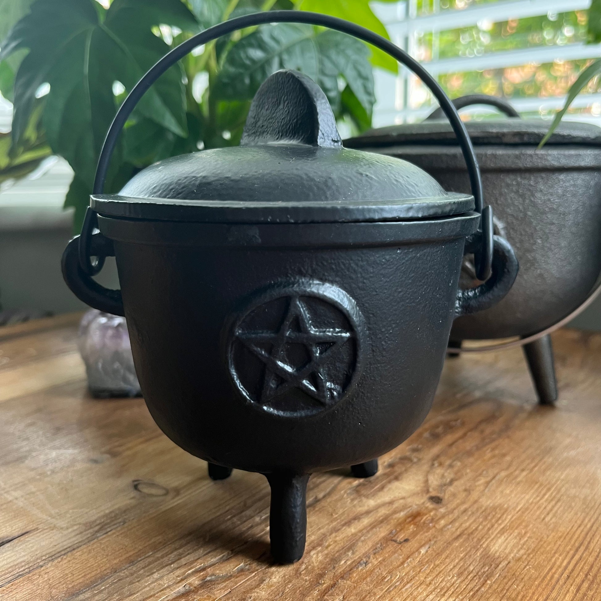 Black cast iron cauldron with a pentagram symbol on a wooden surface.