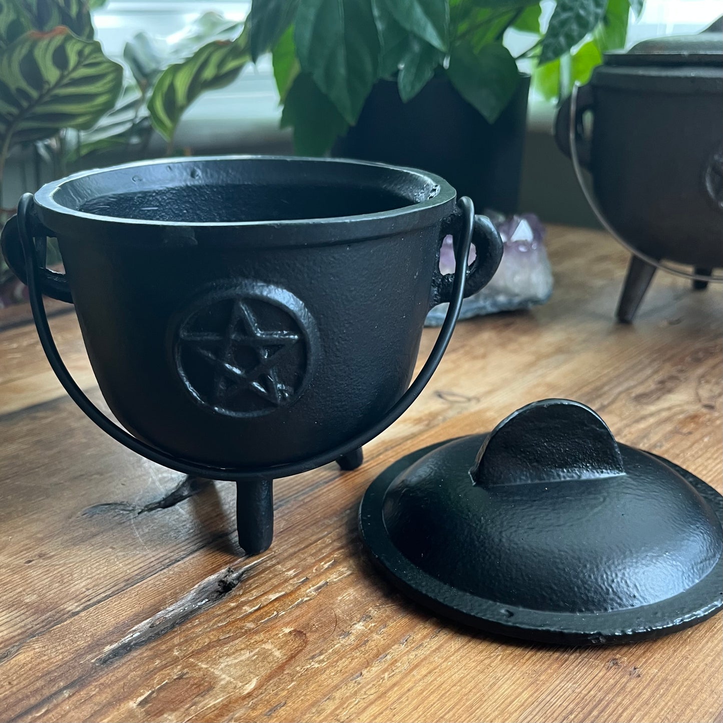 Black cast iron cauldron with a pentagram design on a wooden surface.