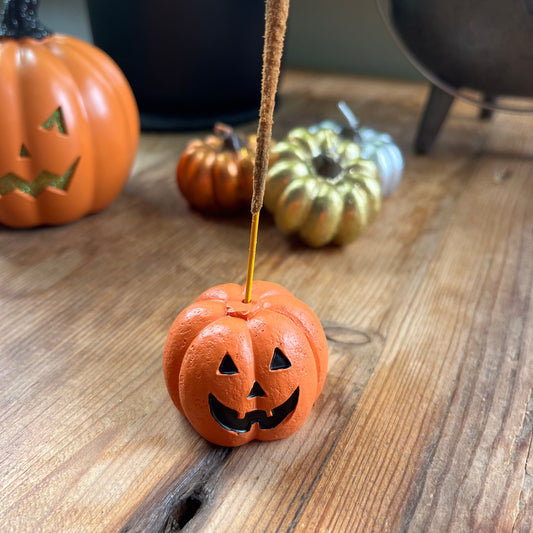 Small pumpkin-shaped jack-o'-lantern with a candle on a wooden surface, surrounded by other pumpkins.