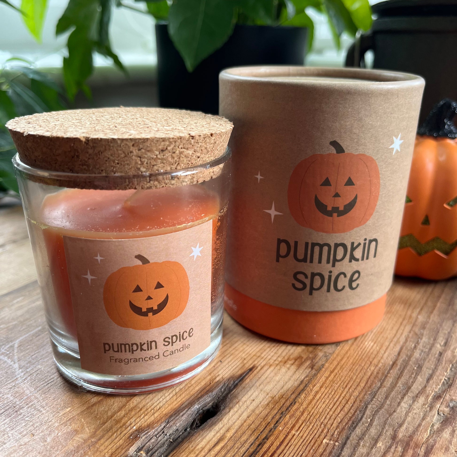 Pumpkin spice candle and container on a wooden surface with Halloween-themed design.