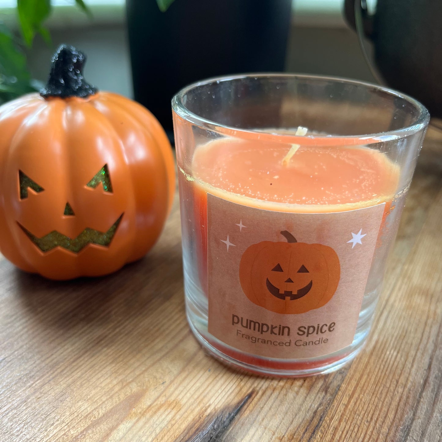 Pumpkin spice candle with a pumpkin design on a wooden surface next to a small pumpkin.