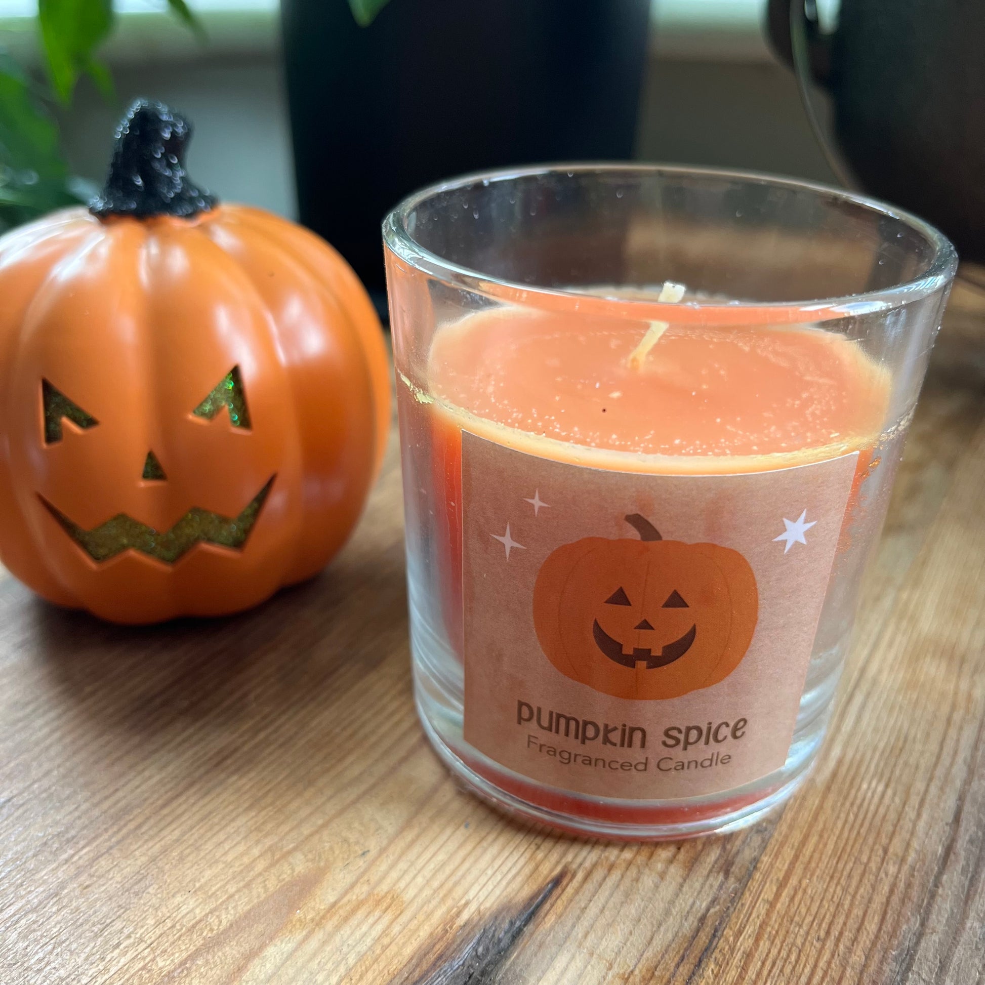Pumpkin spice candle with a pumpkin design on a wooden surface next to a small pumpkin.