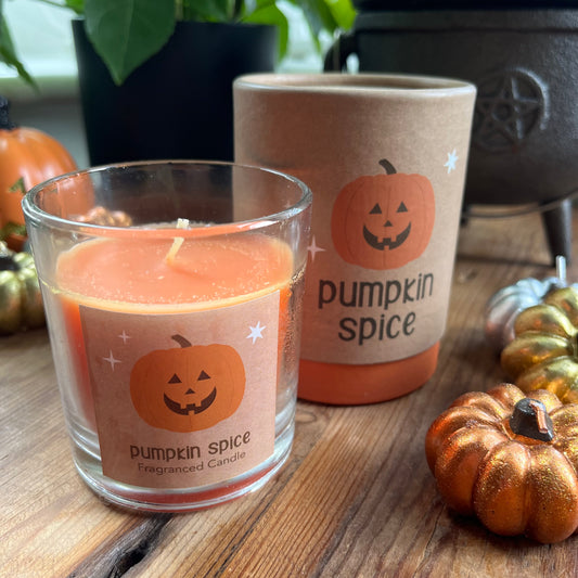 Pumpkin spice candles with pumpkins on labels on a wooden surface.