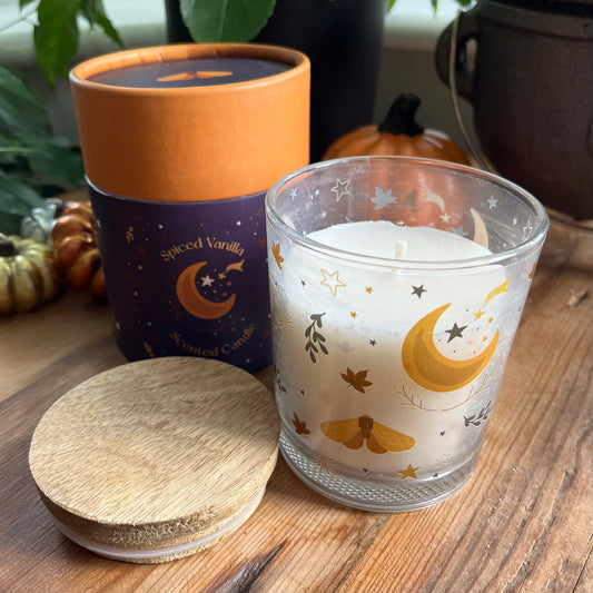 Frosted glass candle with moon and star design on a wooden surface, next to a container labeled 'Spiced Vanilla'.
