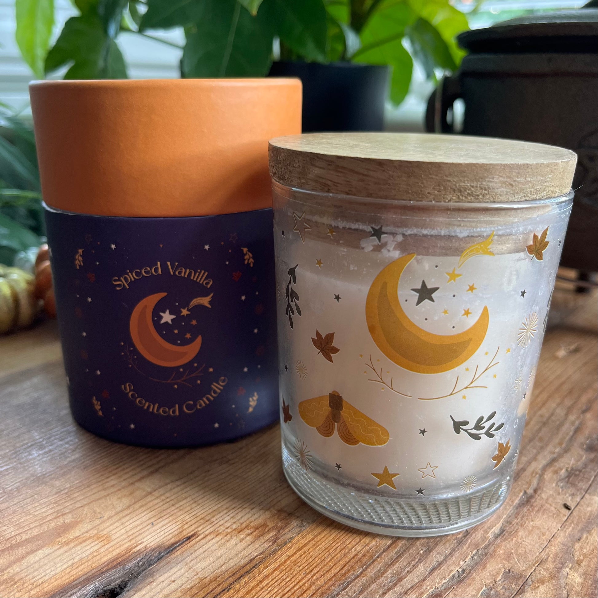Candle in a glass holder with decorative moon & stars design and a cork lid. Next to a cylindrical presentation box labeled 'Spiced Vanilla'.