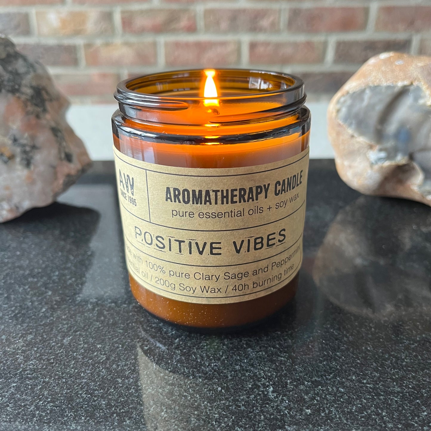 Aromatherapy candle labeled 'Positive Vibes' on a dark surface with a brick wall background.