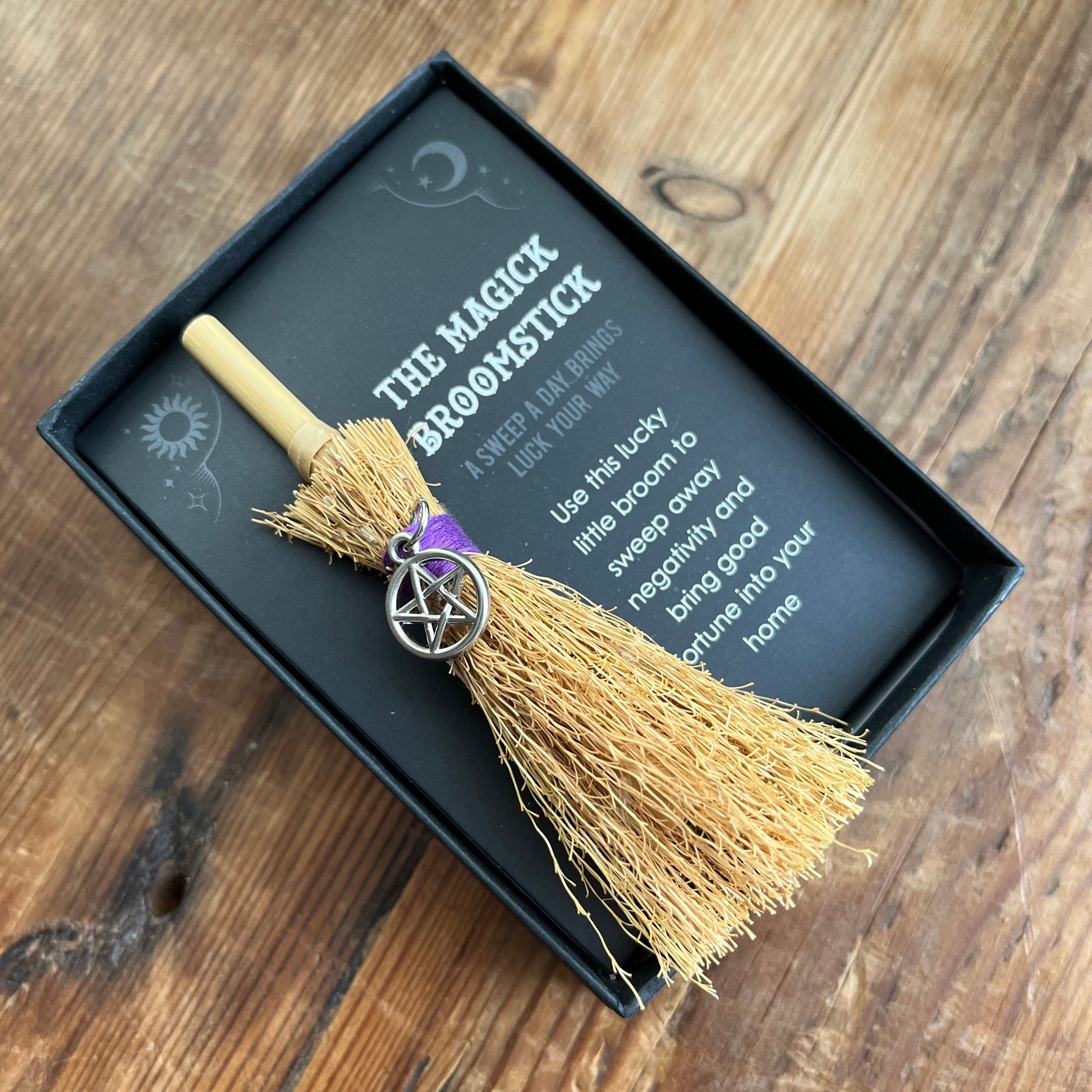Magick broomstick with pentacle charm in a black box on a wooden surface