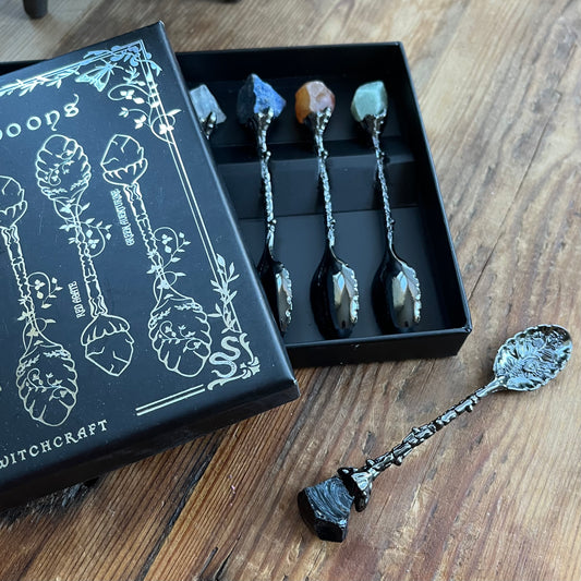 Set of decorative spoons with a black box labeled 'Witchcraft' on a wooden surface.