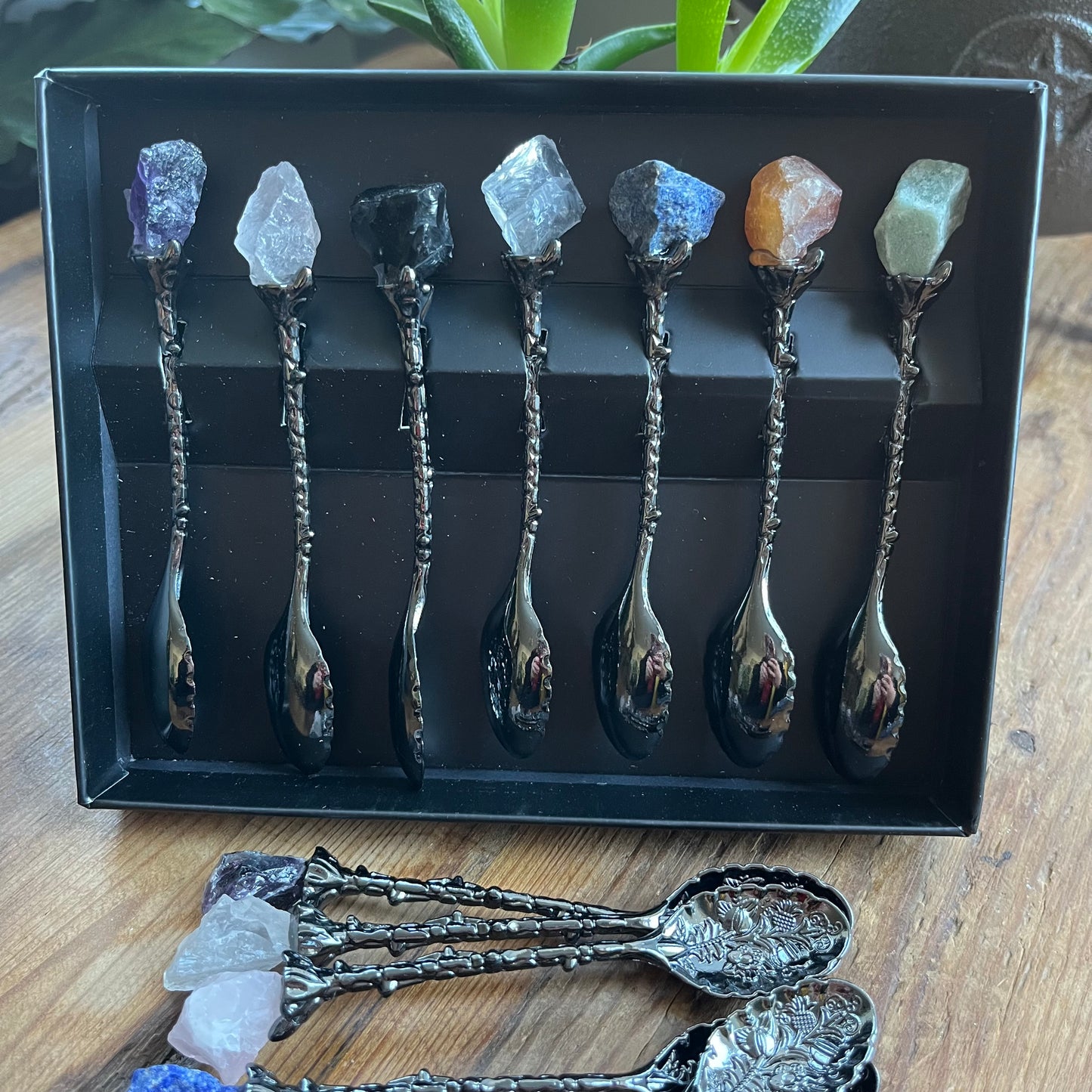 Set of decorative spoons with crystal handles in a black box on a wooden surface.